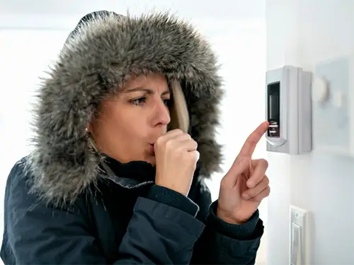 Orlando homeowner wearing a coat indoors and standing by a thermostat waiting for her furnace to be replaced