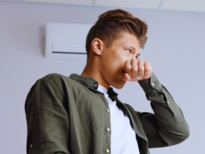 Man covering his nose because of musty smells coming from AC unit